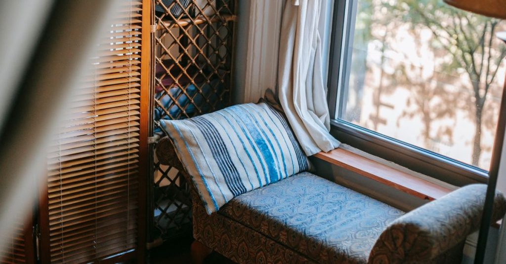 Sudut ruang tamu bergaya vintage dengan sofa yang nyaman, bantal, dan pemandangan jendela.