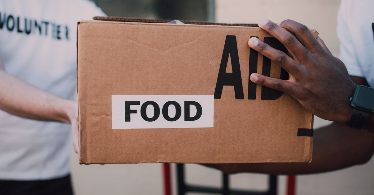 Dua relawan menyerahkan kotak yang diberi label 'Bantuan Makanan', melambangkan dukungan komunitas.