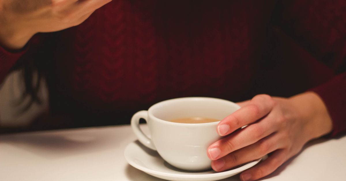 Close-up seorang yang memegang secangkir kopi di dalam ruangan, menciptakan suasana yang cozy dan hangat.