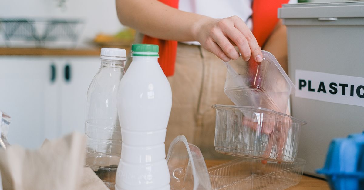 Seorang wanita dewasa mengelompokkan wadah plastik ke dalam tempat sampah daur ulang di dapur.