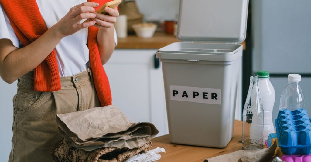 Seseorang menyortir bahan daur ulang ke dalam tempat sampah kertas yang diberi label di dapur.