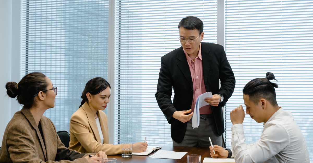 Sekelompok orang dewasa yang beragam terlibat dalam rapat bisnis di dalam kantor modern.