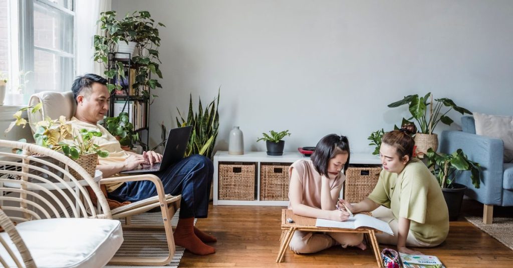 Sebuah keluarga yang terlibat dalam belajar di rumah dengan ayah di laptop dan ibu membantu putrinya dengan pekerjaan rumah.