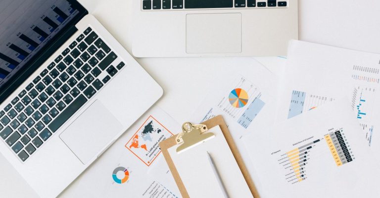 Pandangan dari atas laptop, grafik, dan laporan yang digunakan untuk analisis data di atas meja.