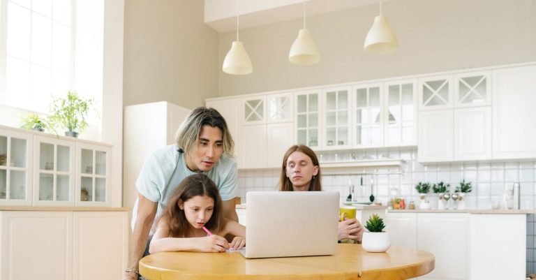 Sebuah keluarga yang terlibat dalam pembelajaran di rumah di sekitar laptop di dapur modern yang cerah, mendukung pendidikan.