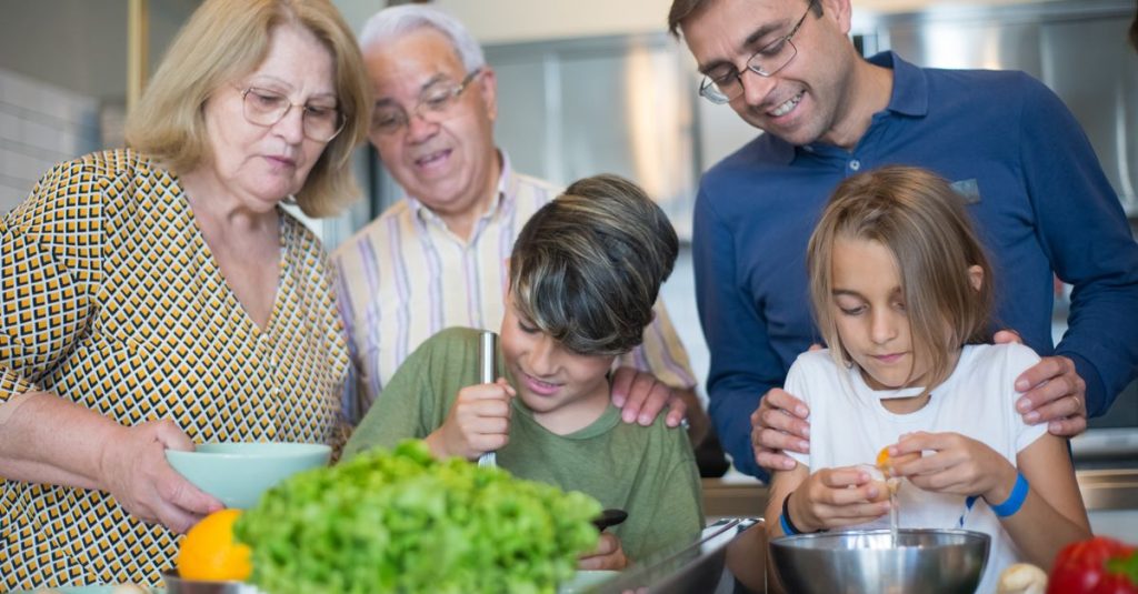 Sebuah keluarga multi-generasi yang ceria saling mengikat sambil menyiapkan makanan di dapur.