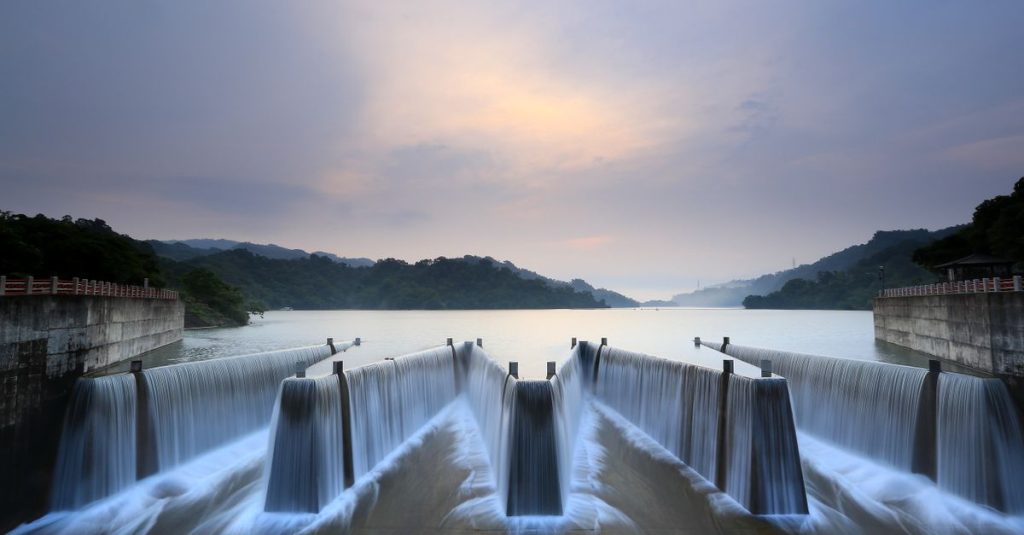 Pemandangan indah dari bendungan hidroelektrik dengan air yang mengalir saat matahari terbit, melambangkan energi terbarukan di alam.
