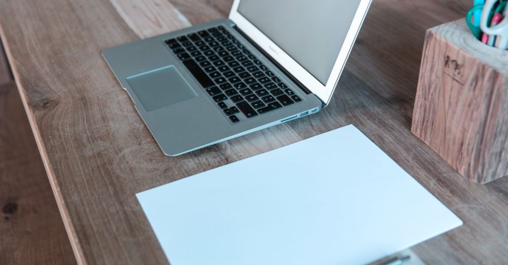 Meja yang bersih dan terorganisir dengan laptop, kertas, dan pena, ideal untuk bekerja atau belajar di lingkungan modern.