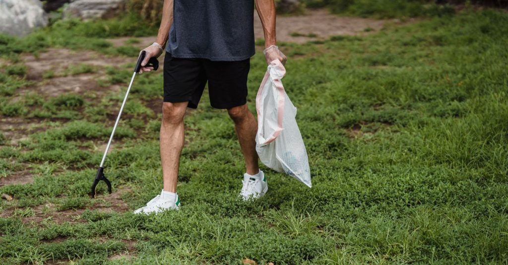 Pria yang memungut sampah di taman dengan sarung tangan dan kantong sampah, mempromosikan praktik ramah lingkungan.