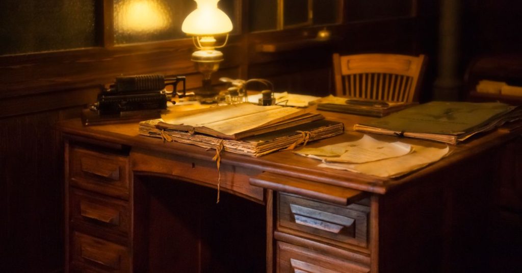 Pengaturan kantor vintage yang nyaman dengan mesin ketik antik, lampu, dan dokumen di atas meja kayu.