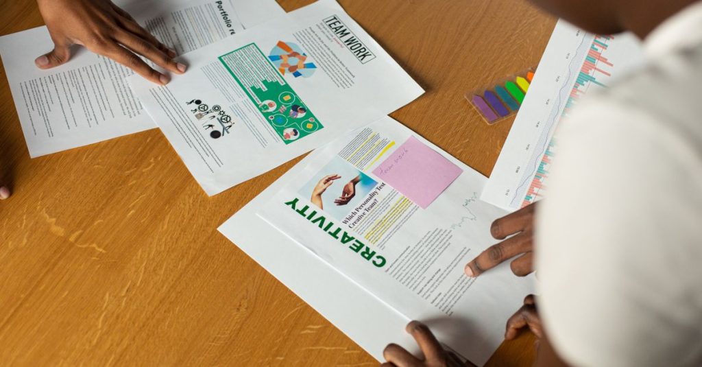 Tampilan atas tim yang beragam berkolaborasi pada dokumen, menyoroti kerja sama tim dan kreativitas.