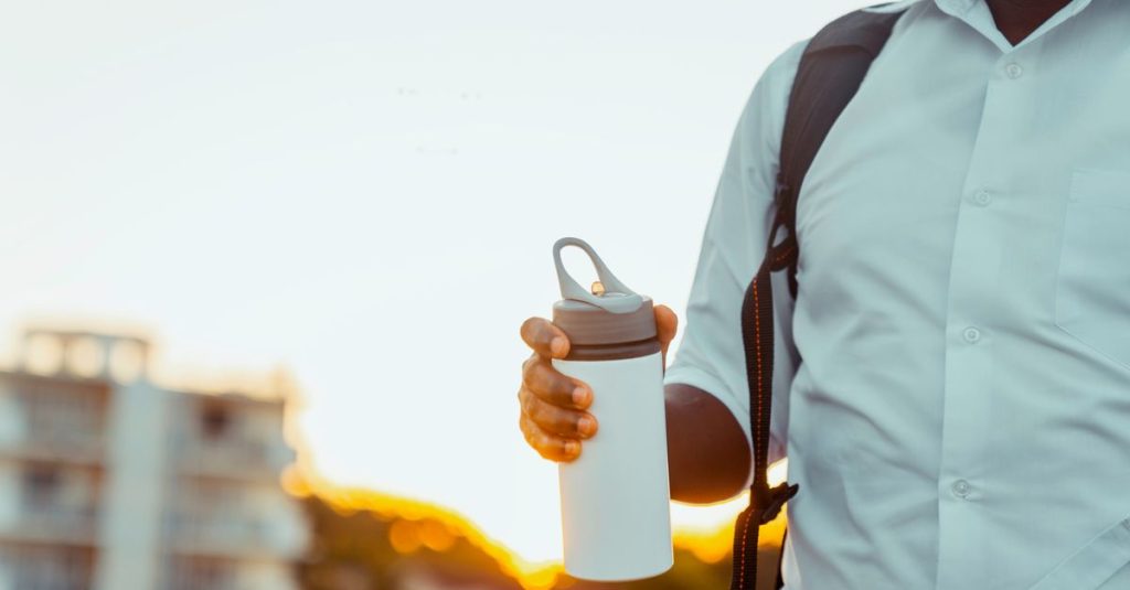 Seorang pria yang memegang thermos dengan ransel, diabadikan di latar belakang matahari terbenam yang cerah di Dar es Salaam.